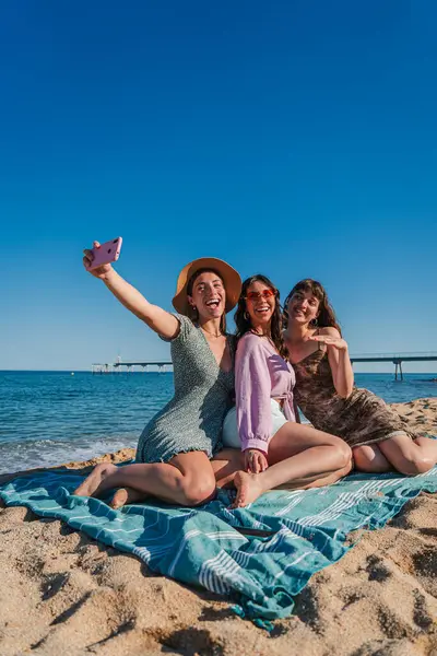 Dikey giyinmiş kadınlar kumsalda uzanmış cep telefonuyla selfie çekiyorlar. Bir grup kız, yaz tatillerinde deniz kenarında gülümseyip akıllı telefonlara poz veriyorlar.