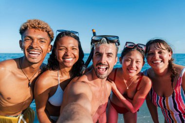 Sahilde yüzerken eğlenen bir grup çok ırklı arkadaşın selfie portresi. Genç yetişkinler, yaz tatillerini hatırlamak için gülümseyip poz veriyorlar. Yüksek