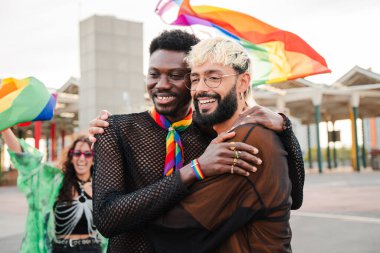 LGBT Onur Yürüyüşü 'nde gülen ve sarılan çok ırklı homoseksüel çiftin portresi. Cinsel çeşitliliği kutlayan ve gülümseyen iki eşcinsel erkek. Lgtbi halk festivali. Yüksek kalite