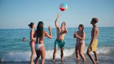 Bir grup genç çok ırklı arkadaş sahilde eğleniyor, şişme bir topla denizde oynuyor ve sahilde yaz tatilinin tadını çıkarıyorlar. Mutlu turistler kıyıda iyi vakit geçiriyorlar.