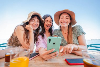 Üç kız sahildeki bar terasında akıllı telefonu izliyor. Sosyal medyada cep telefonuyla eğlenen bir grup genç kadın. Pazar yerinde cep telefonu kullanan kız öğrenciler.