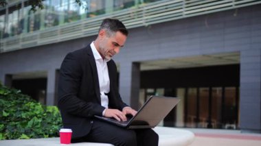 Finans bölgesinde dizüstü bilgisayarla çalışan yetişkin bir iş adamının portresi. Dışarıdaki iş e-postalarına cevap vermek için not defteri kullanan yakışıklı bir orta yaşlı girişimci. Yüksek