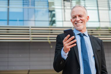 Gri saçlı, iş e-postaları göndermek için cep telefonu kullanan olgun bir iş adamı. MID yetişkin erkek şirket çalışanı cep telefonu uygulaması ile internette geziniyor. Akıllı telefonu olan beyaz yakalı bir işçi.