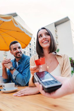 Temassız kredi kartı ödemesini kullanarak kahve dükkanının faturasını ödeyen dikey çift. Genç, yetişkin bir müşteri kadın banka kartıyla bir restoranı kasiyere satıyor. İnsanlar harcıyor