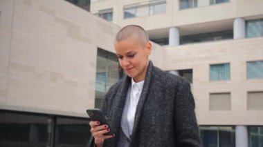 Bir iş kadını iş mesajları göndermek için cep telefonu kullanıyor. Dışarıda akıllı telefonuyla çalışan olgun bir kadın. Şehir merkezindeki iş yerinde yürüyen ve cep telefonuyla mesajlaşan kendinden emin orta yaşlı bir kadın.