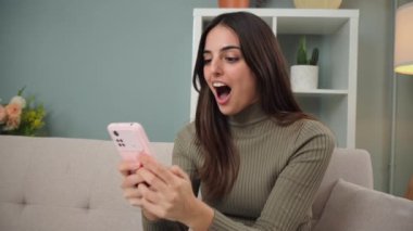 Genç bir kadın, akıllı telefon uygulamasından sonuçları kontrol ederken bir spor bahsini kazandığını kutluyor. İnternet kumarhanesinde cep telefonuyla bahis oynayan mutlu bir kadın. Piyango ödülünü izleyen heyecanlı bayan