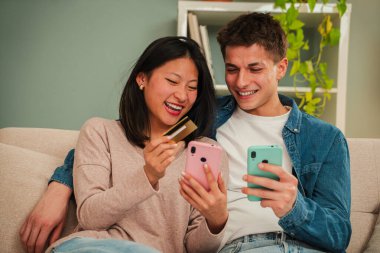 Genç, çok ırklı bir çift evlerindeki koltukta oturmuş internet mağazasında cep telefonu ve kredi kartı kullanarak alışveriş yapıyorlar. Yemek siparişi vermek için cep telefonu kullanan iki kişi. Yüksek