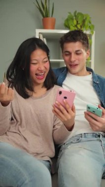 Dikey. Genç, çok ırklı bir çift evlerindeki koltukta oturuyor, bir internet mağazasında cep telefonu ve kredi kartı kullanarak alışveriş yapıyorlar. İki kişi yemek siparişi vermek için cep telefonu kullanıyor.