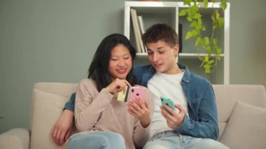 Genç, çok ırklı bir çift evlerindeki koltukta oturmuş internet mağazasında cep telefonu ve kredi kartı kullanarak alışveriş yapıyorlar. Yemek siparişi vermek için cep telefonu kullanan iki kişi. Yüksek