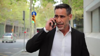 Yetişkin bir işadamı, şehir merkezindeki bir iş yerinde cep telefonuyla konuşuyor ve yürüyor. Orta yaşlı bir adam cep telefonuyla iş görüşmesi yapıyor. Akıllı telefon kullanan başarılı bir erkek.