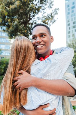 Dikey. Afrikalı Amerikalı bir adam kız arkadaşına şefkatle sarılıyor. Çok ırklı çift mutlu bir şekilde sarılıyor. Erkek arkadaş ve kız arkadaş bir randevuda birbirlerini selamlıyorlar. Birbirine sarılan iki genç insan.