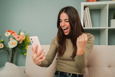 Kadın, akıllı telefon uygulamasından sonuçları kontrol ederken bir spor bahsini kazandığını kutluyor. İnternet kumarhanesinde cep telefonuyla bahis oynayan mutlu bir kadın. Piyango ödülünü izleyen heyecanlı bir bayan.