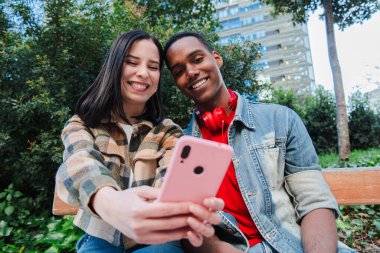 Genç, çok ırklı bir çift cep telefonuyla internette gezinmeyi seviyor. İki genç arkadaş sosyal medya uygulamasında içeriği paylaşmak için akıllı telefon kullanıyor. Gençler cep telefonu ekranını izliyor. Yüksek