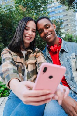Dikey. Genç, çok ırklı bir çift cep telefonuyla internette gezinmeyi seviyor. İki genç arkadaş sosyal medya uygulamasında içeriği paylaşmak için akıllı telefon kullanıyor. Gençler cep telefonu ekranını izliyor