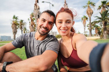 Sportif bir çift spor yaparken çimlerin üzerinde dinlenirken spor yapıyor. Vücut yapılarını geliştirmek için koşu antrenmanlarının bir parçası olarak. Aktif antremandan sonra kameraya bakan iki genç