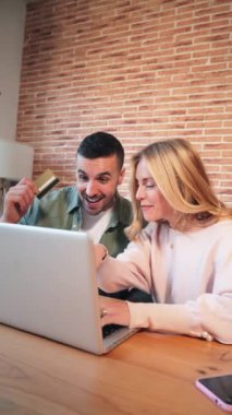 Dikey genç Kafkasyalı çift internetten sipariş vermek ve kredi kartlarıyla ödemek için dizüstü bilgisayar kullanıyor. İnternetten bilgisayarla alışveriş yapan iki kişi, evlerinin oturma odasında oturuyorlar.