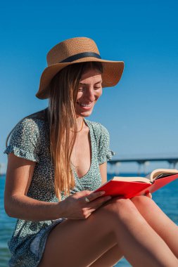 Sahilde oturmuş kitap okuyan genç bir kadın. Sarışın kadın, sahil şeridinde dinlenen edebiyattan hoşlanıyor. Kafkasyalı bir kız tatillerinde deniz kenarında bir romanla rahatlıyor.