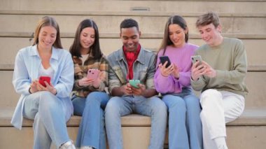 Merdivenlerde oturan, cep telefonlarını kullanarak sosyal medyada fotoğraf paylaşan bir grup çok ırklı genç arkadaş. Ergen öğrenciler bir toplantıda cep telefonu uygulaması ile birlikte oyun oynuyorlar.