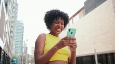 Afrikalı Amerikalı bir kız cep telefonuyla internete girip bir uygulama kullanarak gülümsüyor. Sosyal medyada cep telefonuyla fotoğraf paylaşan genç bir kız. Dışarıda akıllı telefon tutan genç bir kadın. Yüksek