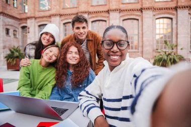 Afrikalı Amerikalı ergen öğrenci, akıllı bir telefonla arkadaşlarıyla selfie çekiyor. Bir grup çok ırklı sınıf arkadaşı arkadaşça bir toplantıda üniversite kampüsünde cep telefonuyla fotoğraf çekiyorlar.