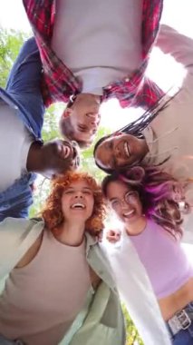 Dikey. Bir grup çok ırklı mutlu gencin birbirine daire şeklinde sarıldığı, gülümseyen yüzlerle, arkadaşlığı, çeşitliliği ve birlikteliği temsil eden kameraya baktıkları düşük açılı bakış açısı.