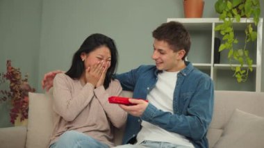 Heyecanlı genç bir kadın, evinde rahat bir kanepede oturmuş rahat bir atmosferde neşe ve mutlulukla özel bir anı kutlarken erkek arkadaşından sürpriz bir hediye açıyor. Yüksek kalite