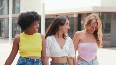 Şehir kaldırımlarında yürürken, alışveriş torbaları taşırken ve tasasız bir şekilde kucaklaşırken gülen ve sohbet eden neşeli bir grup genç kadın. Yeni kıyafetler aldıktan sonra şehir merkezinde yürüyen kızlar.