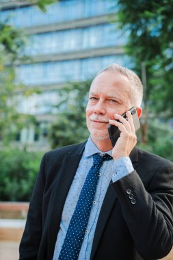 Dikey. Takım elbiseli kendine güvenen işadamı cep telefonuyla konuşurken gülümsüyor iletişim, başarı ve profesyonel bir yaşam tarzı sergiliyor. Erkek iş görüşmesi yapıyor.