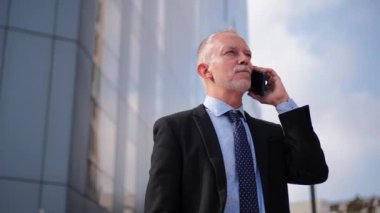 Takım elbiseli kendine güvenen işadamı cep telefonuyla konuşurken gülümsüyor iletişim, başarı ve profesyonel bir yaşam tarzı sergiliyor. Erkek, iş görüşmesi yapıyor. Yüksek kalite