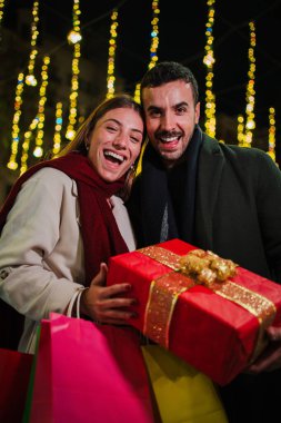 Dikey. Noel hediyesini gece dışarıda tutan mutlu bir çift. Etrafı şenlikli ışıklar ve bayram süslemeleriyle çevrili. Xmas ruhunun tadını çıkarıyorlar. Yüksek