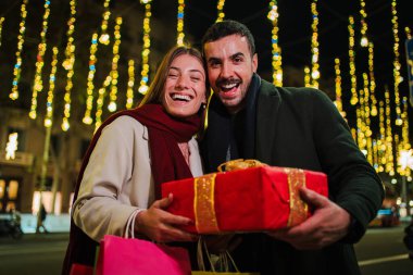 Noel hediyesini gece dışarıda tutan mutlu bir çift. Etrafı şenlikli ışıklar ve bayram süslemeleriyle çevrili. Xmas ruhunun tadını çıkarıyorlar. Yüksek kalite fotoğraf