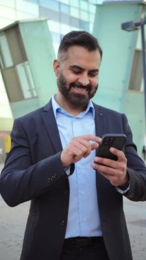 Dikey. Kendine güvenen, olgun bir iş adamı, resmi bir takım elbise giymiş, güler yüzlü, üretken, profesyonel başarıyı, iletişimi ve bağlantıyı gösteren bir cep telefonu kullanıyor.