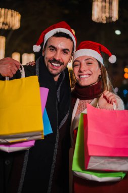 Noel Baba şapkası takan genç ve dikey neşeli bir çift Noel 'i gece açık havada kutluyorlar. Bayram ruhunun keyfini çıkarırken kameraya tatil alışverişlerini gösteriyorlar.