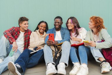 Smartphone 'un mavi bir turkuaz duvarın karşısında oturmasından büyülenmiş çeşitli genç kolej öğrencileri kaynaşıyor ve birlikte bir anı paylaşıyorlar. Gençler cep telefonuyla bakıyorlar. Yüksek