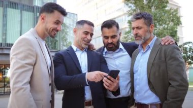 Bir grup işadamı bir cep telefonuna bakarken gülümsüyor ve tartışıyor, bir iş molası sırasında bilgi veya fikir paylaşıyor, takım çalışması, iletişim ve işbirliği gösteriyor. Yüksek