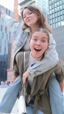 Dikey. Neşeli genç bir kadın, gülerken ve dışarıda eğlenirken arkadaşına sırtına biniyor. Neşeli bir günde mutluluk, dostluk ve neşe dolu anlar yaşıyor.