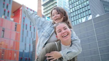 Neşeli genç bir kadın arkadaşına sırtına bindirirken birlikte gülerken ve dışarıda eğlenirken neşeli bir bağ ve gülümseme gününde mutluluk, dostluk ve neşeli anlar gösterir.