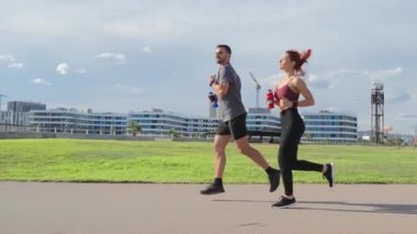 Ağır çekim. Formda bir çift çimenli bir sahada birlikte koşuyor, takım çalışması, fitness motivasyonu ve sabah koşuları sırasında sağlıklı aktif bir yaşam tarzı sergiliyor. Kardiyo ve bacak egzersizi. Yüksek