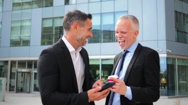 İki profesyonel iş adamı akıllı bir telefona bakarken iş hakkında konuşuyor, bir iş görüşmesi sırasında iş birliği yapıyor ve beyin fırtınası yapıyor, takım elbise giyiyor ve odaklanmış bir tavır takınıyorlar.