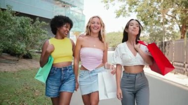 Şehir kaldırımlarında yürürken, alışveriş torbaları taşırken ve tasasız bir şekilde kucaklaşırken gülen ve sohbet eden neşeli bir grup genç kadın. Yeni kıyafetler aldıktan sonra şehir merkezinde yürüyen kızlar.