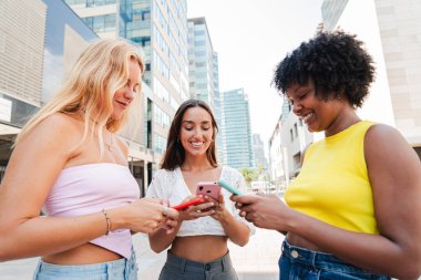 Akıllı telefonlarını kullanan, dostluk ve bağlarını sergileyen, neşe ve mutluluk dolu üç genç kadın. Sosyal medyada cep telefonu başvurusuyla eğlenen bir grup kız.