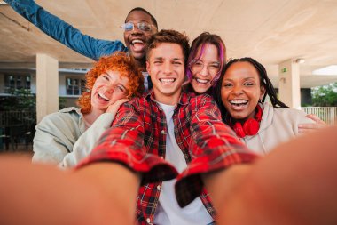 Çok ırklı arkadaşlardan oluşan neşeli bir grup birlikte eğlenceli bir selfie anının tadını çıkarıyorlar. Öğrenciler ve sınıf arkadaşları olarak hayatlarında unutulmaz bir deneyim yakalarken mutluluklarını ve yoldaşlıklarını sergiliyorlar.