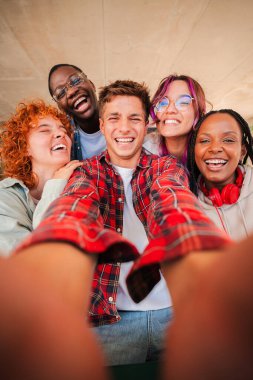 Çok ırklı arkadaşlardan oluşan neşeli bir grup birlikte eğlenceli bir selfie anının tadını çıkarıyorlar. Öğrenciler ve sınıf arkadaşları olarak hayatlarında unutulmaz bir deneyim yakalarken mutluluklarını ve yoldaşlıklarını sergiliyorlar.