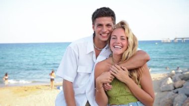 Neşeli genç çift, güzel güneşli bir günde okyanusa karşı gülücüklerle kucaklaşıyorlar, iki insan sahilde yaz tatilinin tadını çıkarıyorlar. Sahil kıyısındaki arkadaşlarının portresi. Yüksek