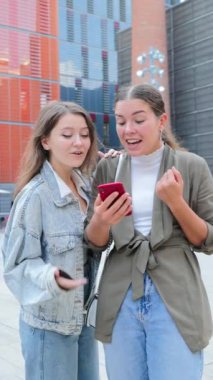 Dikey. Zaferlerini kutlayan iki kadın cep telefonlarında bahis başvurusu yaparken kazandıktan sonra heyecan ve neşe gösteriyorlar, online bahsin heyecanını vurguluyorlar,