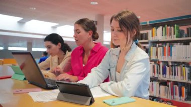 Bir kütüphanede birlikte çalışan, laptopları ve kitaplarıyla çalışmalar yapan, pozitif ve motive edici bir eğitim ekibi kuran üç genç kadından oluşan bir grup.