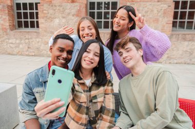 Eğlenceli bir selfie çekerken keyifli bir anın tadını çıkaran, özgün gülümsemeler ve kahkahalar gösteren, Arkadaşlığın ve Neşeli Beraberliğin Özünü Kusursuz bir şekilde yakalayan bir arkadaş grubu