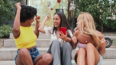 Bir grup kız akıllı telefona bakıyor ve online bahis kazanmamızı kutluyorlar. Üç başarılı genç kadın bir cep telefonuna bakarken bağırıyor, tezahürat yapıyor ve yumruklarını kaldırıyor. Başarı