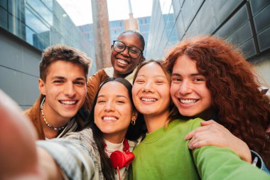 Canlı bir açık havada Neşeli Anları Paylaşan Çeşitli Genç Arkadaşlardan oluşan bir grup Parlak Gülümsemeler ve Parlak İfadelerle Birlikte Eşsiz Bağlarını ve Mutluluklarını Yakalarken Selfie çekiyorlar.