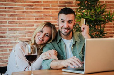 Mutlu çift kameraya gülümserken bir kredi kartıyla internetten alışveriş yapıyor. Rahatlamış bir akşam deneyimi için dizüstü bilgisayar kullanıyorlar ve birbirlerine eşlik ediyorlar. Yüksek